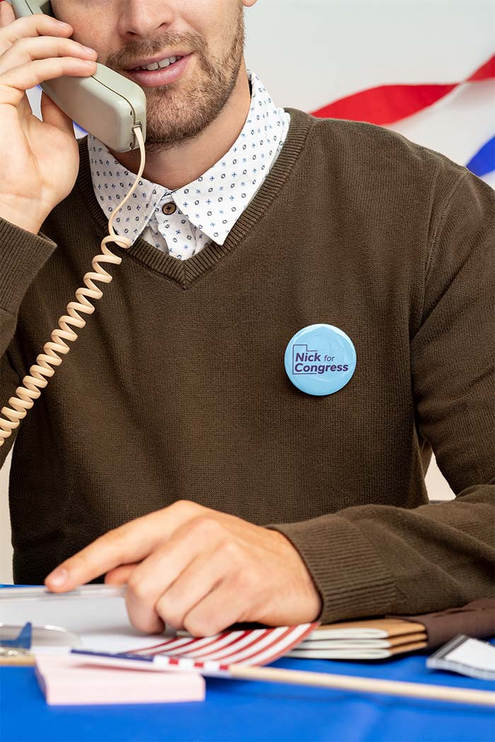 Photo of a man on the phone wearing a blue Nick For Congress Button