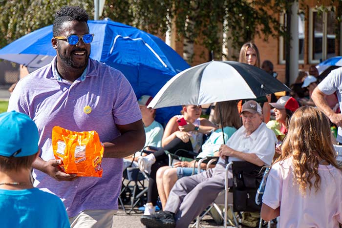 Man in purple shirt passing out candy at a parade