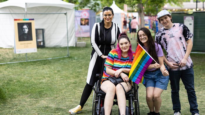 Group of four people posing for a photo in the exhibit while one of them holds a rainbow flag.