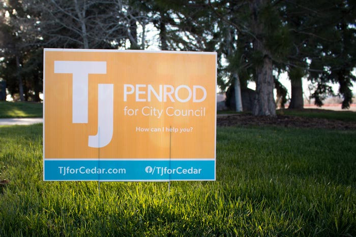 A campaign sign with a golden background with the TJ for Cedar logo and turquoise accent