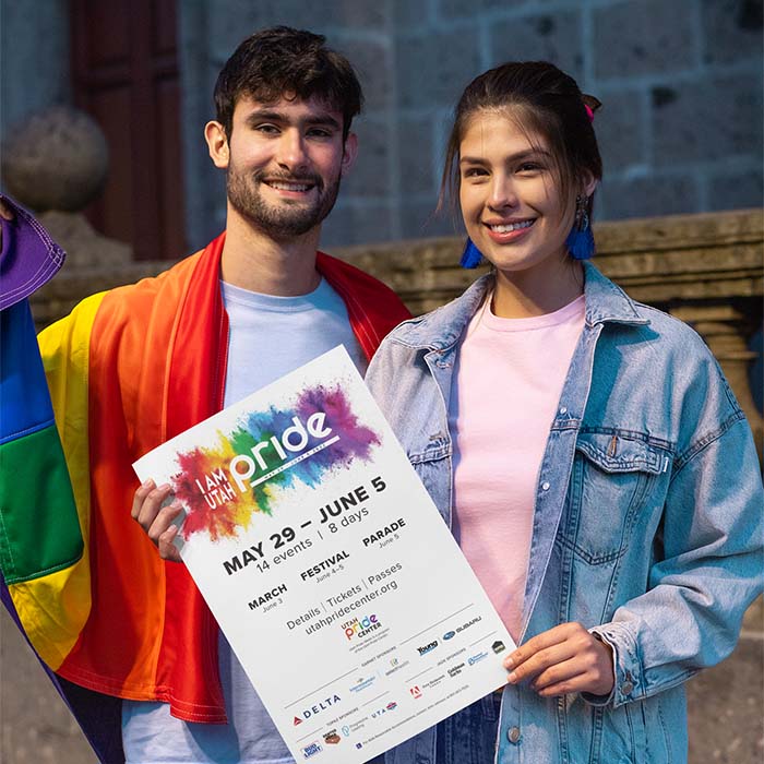 Two people standing outside holding the Pride poster