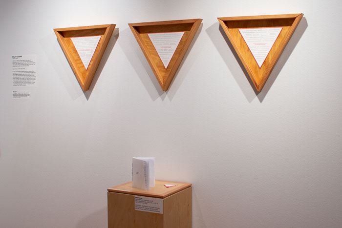 Photo of three triangular frames on the wall with a pedestal holding a book and stickers in the center