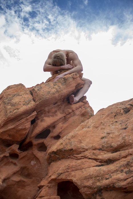 A photograph of a nude man wrapped around a stone resembling one of Goblin Valley's mushroom formations
