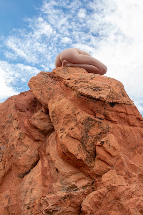 A photograph of a nude on top of a stone resembling one of Goblin Valley's mushroom formations