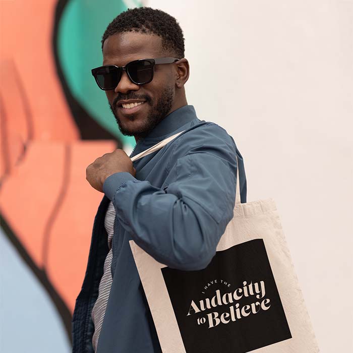 Man wearing a tote bag with the text 'I have the Audacity to Believe'