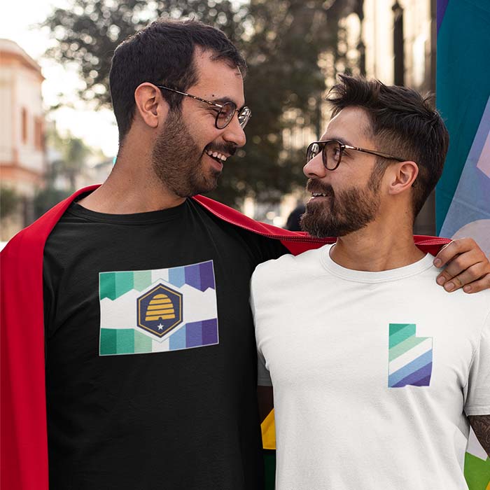 Two men wearing shirts with the new Utah flag with the gay flag colors overlayed