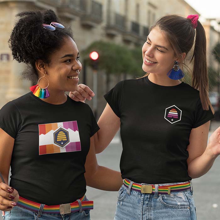 Two women wearing shirts with the new Utah flag with the Lesbian flag colors overlayed