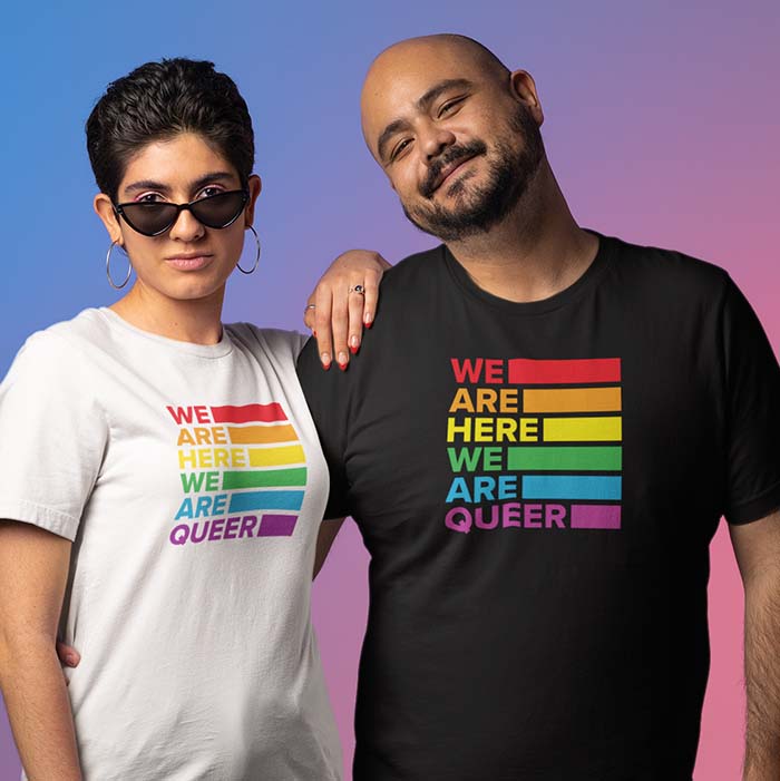 Two people wearing shirts that say 'we are here, we are queer'