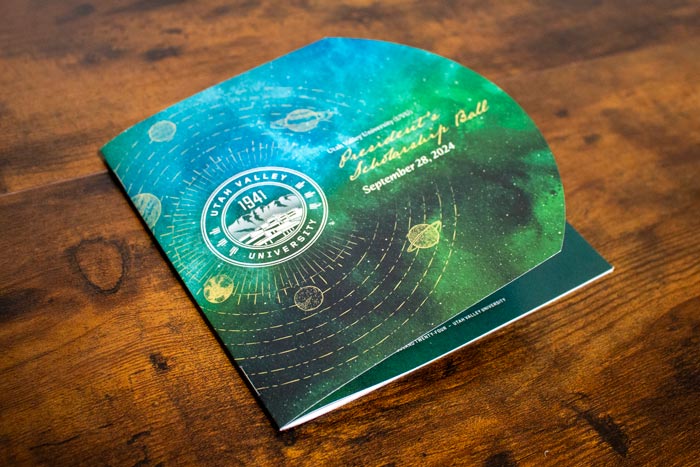 Image of a program on a desk. The front page has a circular die cut which reveals the page beneath.